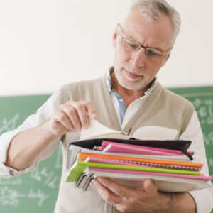 senior-teacher-checking-notepads-classroom
